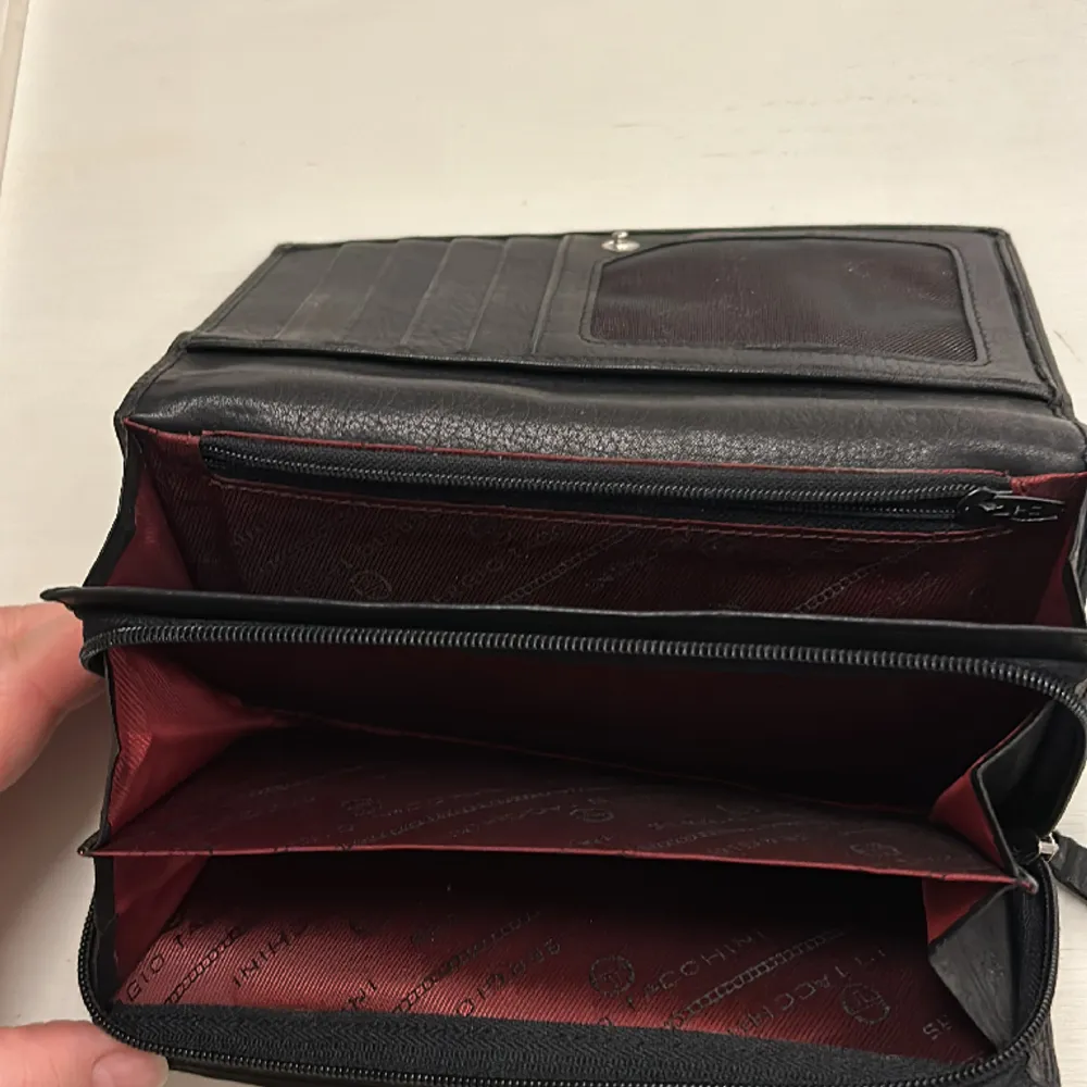 Äkta Sergio Tacchini plånbok i läder med mycket plats för kort. Fack med dragkedja för mynt och loggotext inuti. Fack på sidan och baksidan. . Övrigt.
