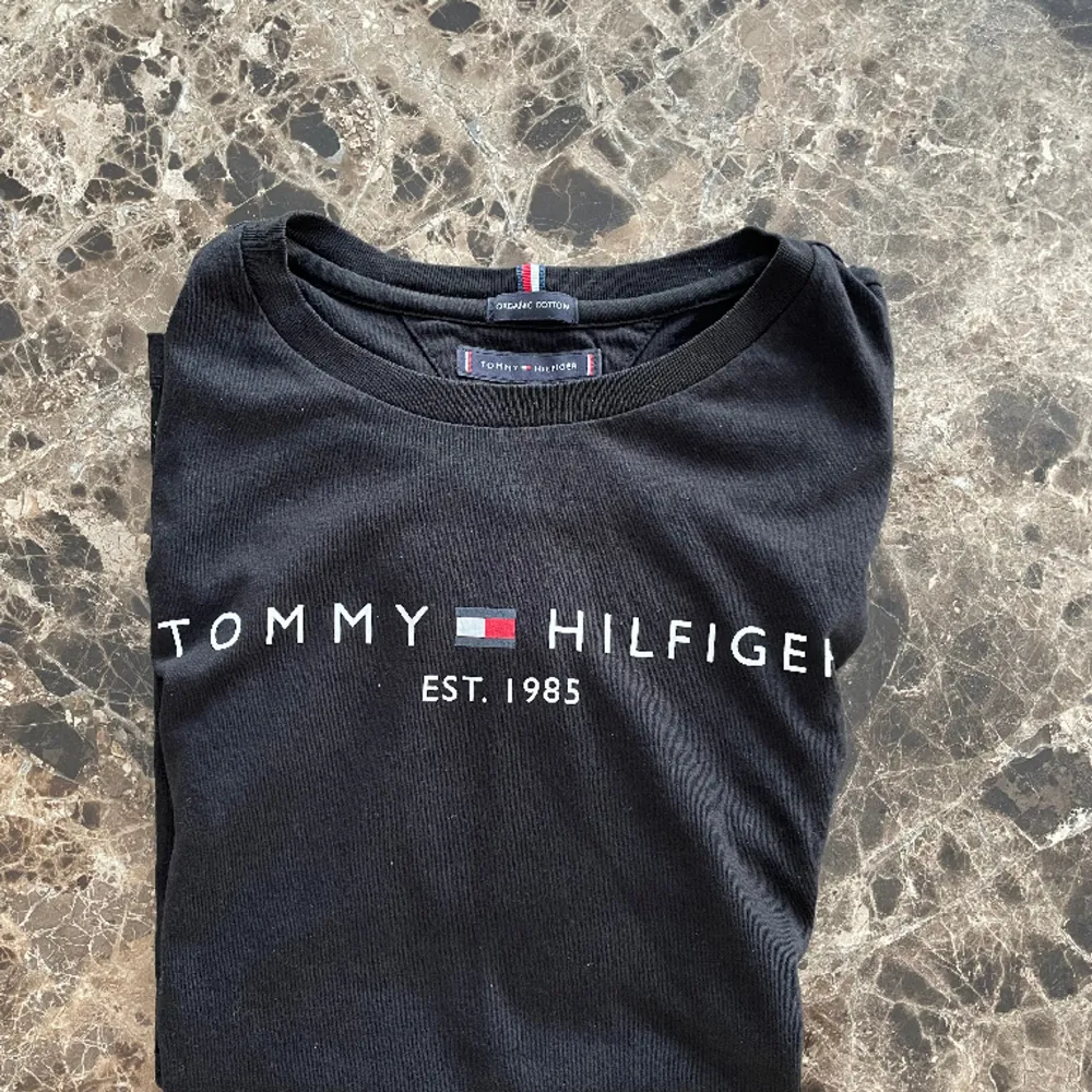 En svart T-shirt från Tommy Hilfiger i mycket gott skick. Bilden på denna annons blir dålig för någon anledning, originella bilden kan skickas via DM.. T-shirts.