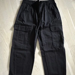 Byxor - Svarta byxor från Nelly, NLY TREND.  Cargo byxor. Fickor på utsida lår på båda benen. Spänne nere vid vristen som detalj och kunna styla hur du vill byxan skall sitta på. 