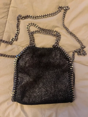 Stella McCartney väska - Intressekoll på min fina stellamccartney väska i modellen tiny. Färgen är svart med glitter och är i bra skick förutom att lite glitter gått bort på baksidan som man kan se i sista bilden. Men inget som syns på.💕tänka mig  att byta mot en glam lock väska