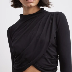 Topp från NAKD - Långärmad svart tröja från NAKD i storlek M. Croppad, ”omlott”, hög i halsen med knäppe bak. Skönt och mjukt material. Normal i storlek. Aldrig använd, endast provad. 