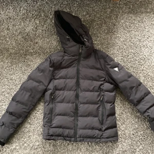 Vinterjacka från Guess - Skön vinterjacka i bra skick. Det enda felet är ett litet hål vid vänstra armen, se bild. 