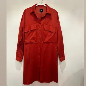 En läcker orangeröd skjortklänning från NÜ Denmark. Skjortklänning kan även användas uppknäppt som en kimono över andra plagg. En riktigt favorit i garderoben som kan användas året om. 