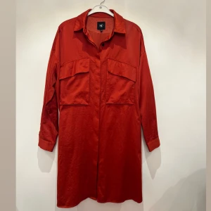 Skjortklänning  - En läcker orangeröd skjortklänning från NÜ Denmark. Skjortklänning kan även användas uppknäppt som en kimono över andra plagg. En riktigt favorit i garderoben som kan användas året om. 