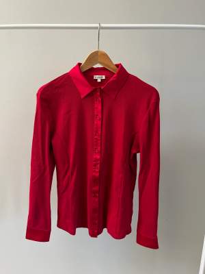 En rosa/röd skjorta från Kettlewell. I 95% bomull och 5% elastan. Har själv köpt den begagnat men har bara använt den två gånger så i fint begagnat skick.