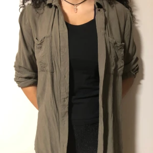 Tunn grön skjorta - Tunn militärgrön skjorta från HM, lite oversized på mindre storlekar men inte så stretchy i t.ex armar. Går att vika ner armar.