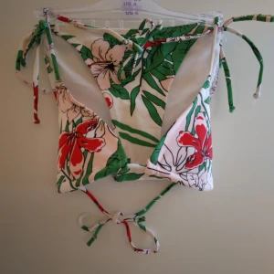 Oanvänd vit tropisk mönstrad bikini, överdel+underdel. Strlk: 34/XS. Felfri. - Oanvänd vit tropisk mönstrad bikini, överdel+underdel. Knyts i ryggen, nacken samt i sidorna på byxan. Strlk: 34/XS. Felfri.