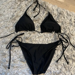Svart bikini  - Svart bikini med extra långa band som går att knyta flera varv runt midjan. Toppen har inlägg som går att ta ut. Storlek S 