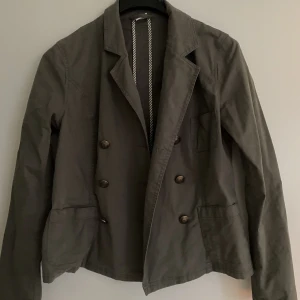 Höst/vår jacka - Snygg grå jacka. Skulle säga att den känns som mindre än 42, den är lite lite stor på mig som vanligtvis bär S. Men sitter fortfarande bra, och är perfekt med en tjockare tröja under. Går precis ner till rumpan. Tunnt men skönt material. Jättebra skick!
