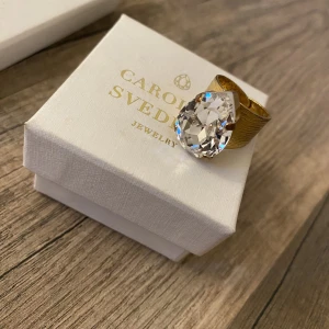 Ring från Caroline Svedbom  - Jätte fin guld ring med klar diamant från Caroline Svedbom. Ringen har lite slitage på insidan men inget som syns när ringen är på. Även piggarna som fäster diamanten är något missfärgade. Ringen är justerbar. Ordinarie pris 595 kr. Asken medföljer🌟
