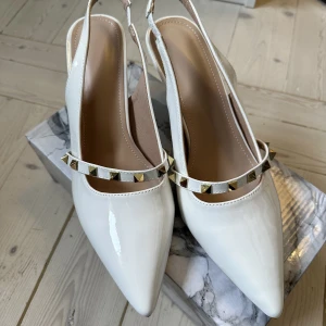 Vita slingbacks med klack - Ursnygga slingbacks med låg stilettklack, lätta att gå i🤍Vita klackar med guldnitar och trendig spetsad tå. Nyskick! Endast prövade inomhus, aldrig använda. 
