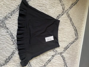 Svart kjol med volang - Svart minikjol med volang längst ner. Kjolen har en liten dragkedja vid. Aldrig använd från NA-KD, storlek 36.