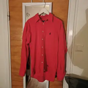 Röd Ralph Lauren Skjorta, prislappen är kvar. Osäker på storleken eftersom det endast står 16 ½, enligt mina mått är axelbredden ca 49 cm och längden 69 enligt mig översätts det till Large. Skriv till mig vid övriga frågor eller liknande. 