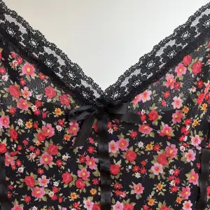 Superfin vintageklänning från 90-talet, inköpt på VintageSphere i Stockholm. Blommigt rosa/rött mönster, svarta spetsdetaljer och svart rosett. Klänningen har något av en drop-waist och korsettdetaljer. Perfekt skick, inga fläckar eller defekter. 