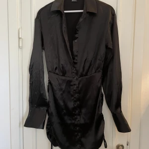 Satinklänning med detalj - Svart satinklänning med långa ärmar. Fina detaljer och passar perfekt för fest. 