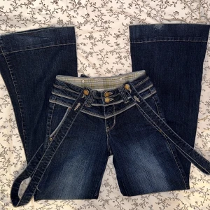 Lågmidjade flare/boocut jeans - Säljer ett par jättecoola lågmidjade flare/boocut jeans med hängslen från 2000-talet, hängslena går att ta av och ljustera lite, väldigt många snygga detaljer, storlek 36 men passar 34 också, väldigt stretchiga så väldigt sköna, unika och ovanliga, långa