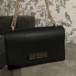 Love-Moschino handväska - Handväska (äkta) med guldfärgad kedja & bokstäver. Använt ett fåtal ggr, i princip nyskick. Bredd: 10 cm Höjd: 6 cm, kedjan går att justera till att bara ha ett band eller 2 på axeln. Den är även av äkta skinn. 🫶🏻