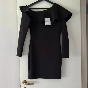 Ny Klänning  - Ny klänning med etiketten kvar. Svart och en fin detalj vid axlarna. 