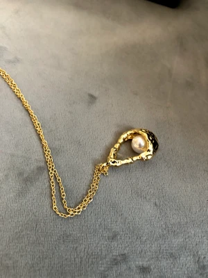 Guldhalsband med sötvattenpärla - Guldpläterat silverhalsband med ingjuten sötvattenpärla i hög kvalitet. Ca 25 x 20 mm långt hänge. Kedjan är 44 cm med möjlighet till förlängning på ytterligare några centimeter. Skön och stadig tyngd. Säljer även matchande örhängen.