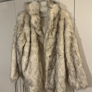 Fuskpäls jacka  - Aldrig använd fuskpäls med huva. Stängs med tryckknappar och har två fickor utan dragkedja. 