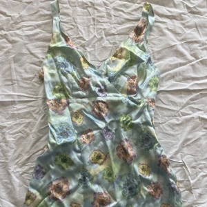 Blommig satin klänning - Väldigt söt satin klänning med blommor på. Lite stor där bak men fixat med litet snöre inuti klänning (kan alltid tas bort) 