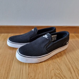Nike skor  - Nike Toki low slip-on  Super fina använda 1 gång.  Färg: Black/White  Produktdetaljer Material: Textil Sula: Gummi Passform: slim fit 
