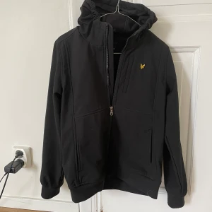 Lyle & Scott Soft Shell Jacka  - Vind- och regntålig svart vår / höst-jacka, med fleecefodrad insida.  Min 14 åring har växt ur den, jackan har funkat jättebra i ett drygt år. Ser fortfarande nästan ny ut, fantastisk kvalitet. Priset är exklusive ev frakt 