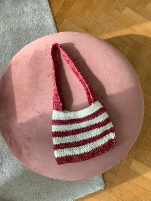 Virkad väska - Hej! Jag säljer en handvirkad röd-och-vit randig väska. Väskan mäter ca 29 x 23 cm, med en axelrem som mäter ca 66 cm. Går att bära både som axelväska och cross-body. 
