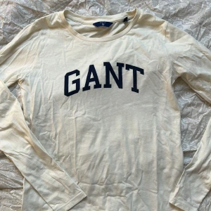 Gant tröja i storlek xs - Jättefin och skön tröja, är långrak i modellen! Lite tunnare tröjor vilket gör den sval, tröjan är off white med marinblå text