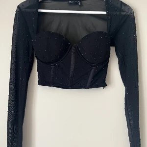 Festtopp  - Festtopp med glittrande svarta stenar. Mesh tyg. Korsett med kupor. Supersnygg. Aldrig använd! Mycket bra skick. Rök och djurfritt hem. 