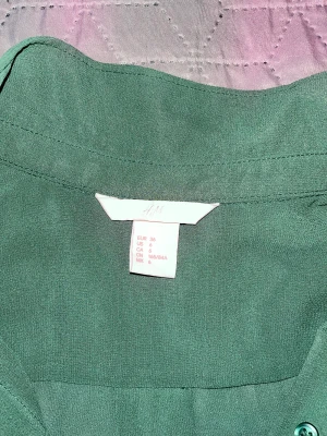 Skjorta  - Grön skjorta utan armar. Lätt tyg till sommaren. Köpt från H&M. Sparsamt använd. 