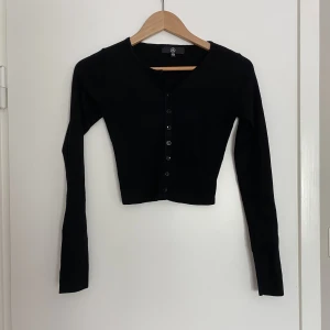 Svart koft-topp från Urban Outfitters - Supersnygg croppad topp i koftmodell! Supersnygg att ha med bara några knappar knäppta i mitten 