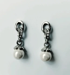 Örhängen - Pärlörhängen med små glittrande stenar på det stjärnformade pärlhänget och länken i mitten. Inköpta på Glitter, aldrig använda. I vitmetall och ca 2,5 cm längd/ höjd.