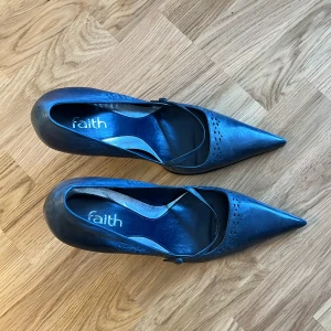 Klackskor från Faith - Jättefina klackskor från det eftertraktade skomärket Faith. Med en spetsig tå, lite hål-detaljer och ett spänne över foten. Jättesnygga både till jeans och kjol. Perfekt till i sommar! Skicket är tipptopp!