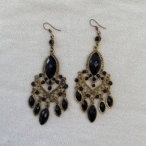 Örhängen med svarta stenar - Säljer detta fina par örhängen köpta i en smyckesbutik utomlands då jag inte använder dem längre. Fint skick. Mörkare guldig färg med svarta stenar.