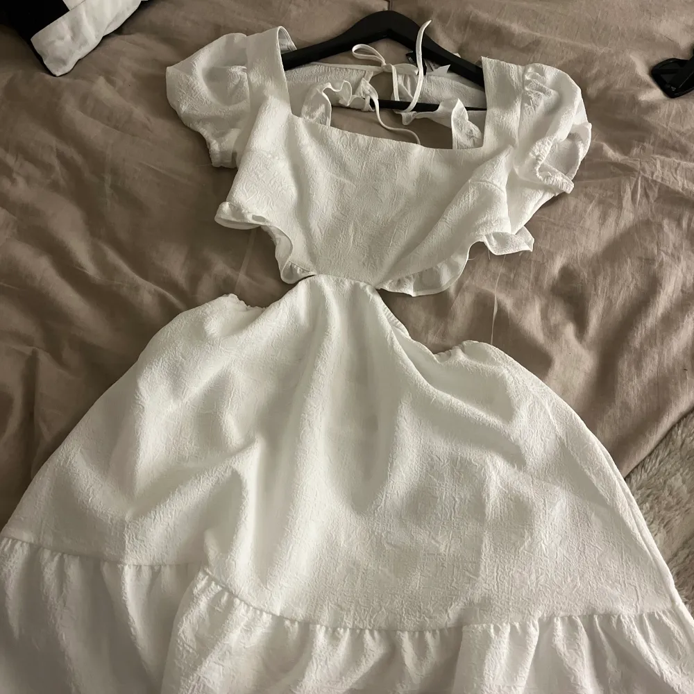 Hej jag säljer en vit klänning som är oanvänd och lappen finns kvar på klänningen, den är öppen i ryggen och vid sidorna av magen men de finns genomskinliga snören som håller upp den.. Klänningar.