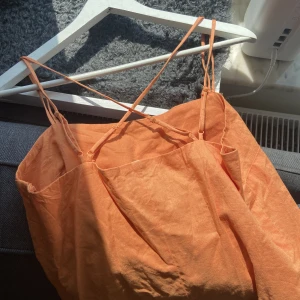 Orange linneklänning - Somrig klänning med justerbara korsade band i ryggen. Svårt att få med färgen på bild, men på första bilden är färgen så gott som rättvis. 50% linne, 50% bomull. Finns gragkedja i sidan. Kortare på mig som är 175cm. Aldrig använd. 