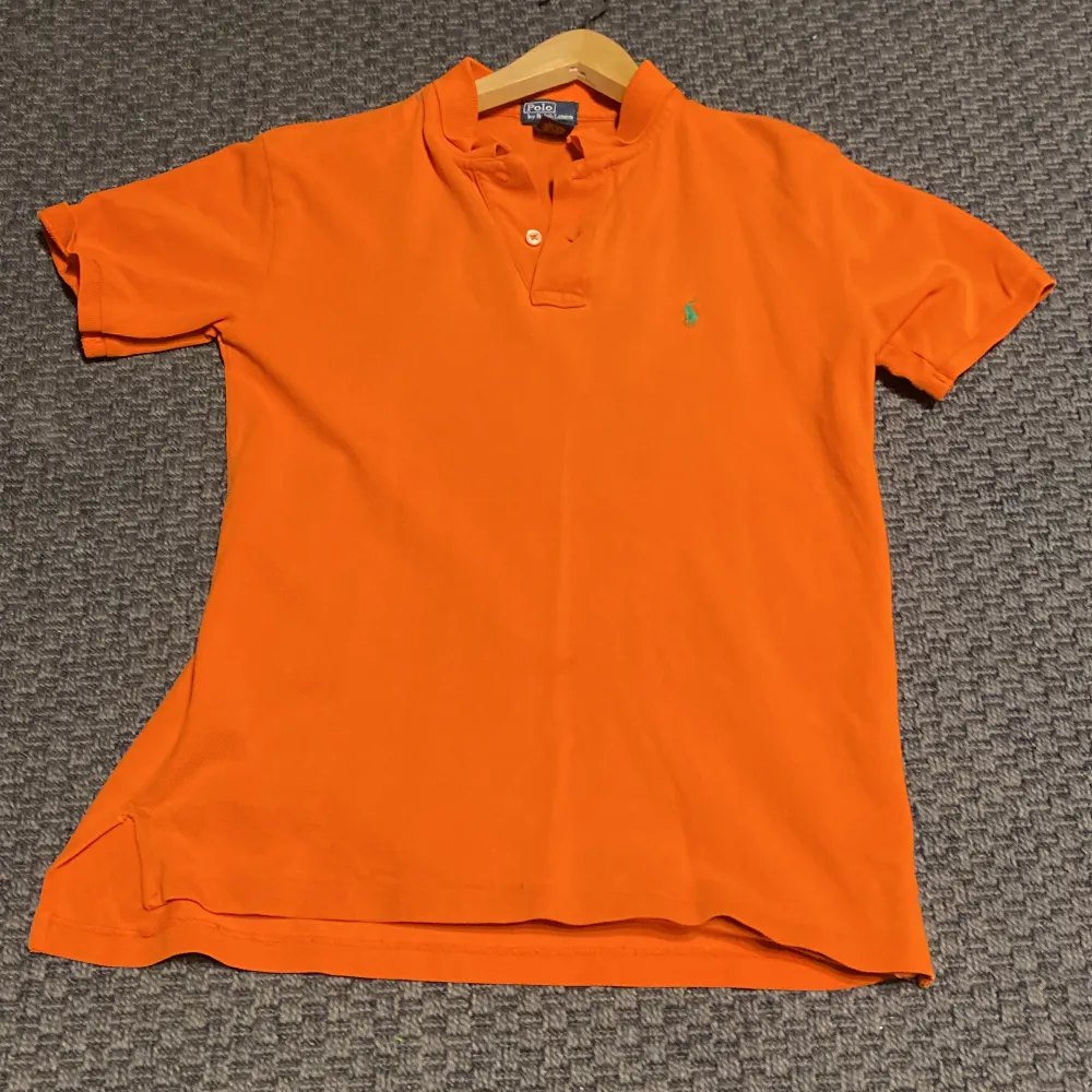 Polo Ralph Lauren tröja i orange. Storleken är medium. En knapp saknas men borde vara enkelt att fixa, sedan litet märke vid nedre delen av tröjan. Det borde ej synas. Skick 7/10. Diskuterbart pris. . T-shirts.