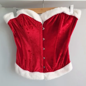 Korsett - Julkorsett gjord i ett sammetsliknande material. Har en viss struktur. Skulle säga att den är mer en M eller en mindre L i storleken. Har aldrig blivit använd och är därför helt i nyskick.