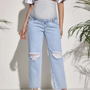 Gravidjeans - Ljusblåa gravidjeans med slitningar på knän och grått tyg över magen. Aldrig använda. Storlek M.