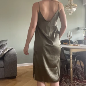 Klänning siden  - V-ringad klänning som faller snyggt, med smala axelband & diskret slits, material 100% polyestersiden. Strl S, använd ett par ggr.   Ps. se att jag klippt bort sömn innanför byst pga syntes utanpå. 