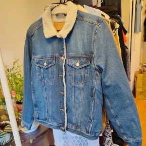 Jeansjacka flufffoder - Blå jeansjacka med vitt flufffoder på insidan av överkroppen. Den är i fint skick, använd en gång. Storlek S.