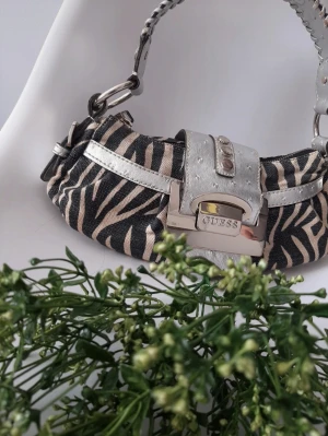 Äkta Vintage Guess väska - 31cm×14cm, lite ytslitage på rem som förväntat på en äldre väska, i övrigt är väskan i kanonskick. Beige, svart + silver. Glöm inte att kolla övriga annonser