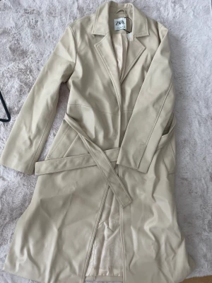 Kappa i läderimitation  - Beige lång kappa i läderimitation. Aldrig använd. Slim 