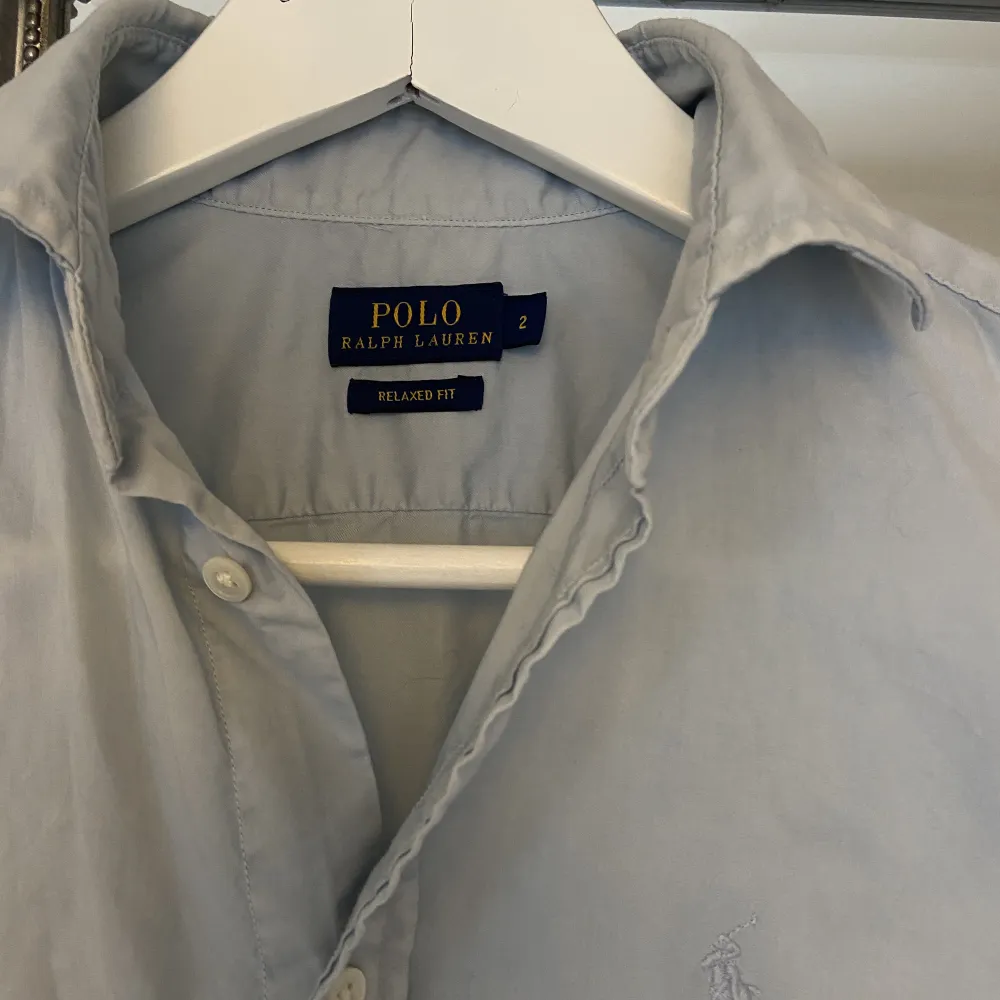 Superhärlig och somrig Ralph Lauren skjorta i ljusblått med ljusblåa knappar i storlek 2 (motsvarande stl. 36). Helt oanvänd. . Skjortor.