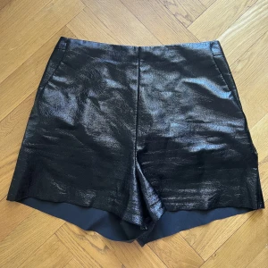Shorts i skinnimmitation  - Kommer ej till användning. Har dragkedja i sidan och fickor fram. Inga fickor bak. 