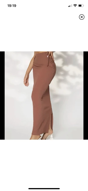 Långkjol med slits - oanvänd -  Oanvänd kjol med slits i baksidan. Den har två knytning pa bägge sidorna som man själv kan justera. Köpt för 250kr, säljer för 130kr. Priset kan diskuteras & den är ljusbrun🤎