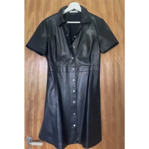 Klänning i konstläder - Kort skjortklänning från Mango.  Konstläder med markerad midja och tryckknappar.   Strl M. Fint skick. 