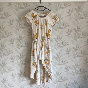 Klänning - Klänning med insydda shorts. En vit klänning med gula blommor på. Längre bak än fram.