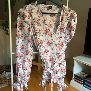 Blommig omlottblus - Jättefin omlottblus, supersnygg till jeans tex. Volang på ärmarna vid handleden, oanvänd. 